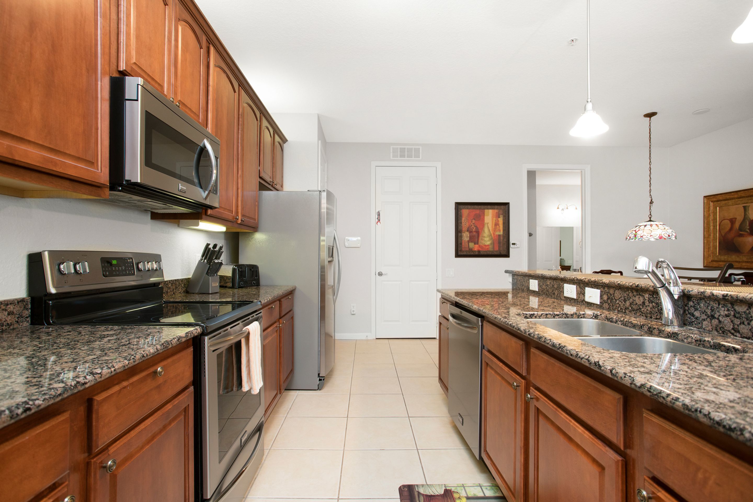 A modern kitchen with wooden cabinets, stainless steel appliances, granite countertops, and a tiled floor.