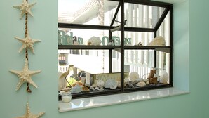Une vitrine présentant diverses coquilles et étoiles de mer, une pancarte sur laquelle on peut lire « La vie, c’est la plage », et une vue sur une clôture blanche et des bâtiments à l’extérieur.