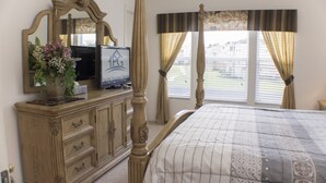 A bedroom with a four-poster bed, a dresser with drawers, a television, and a mirror. - Windsor Palms 8112 (Kissimmee)