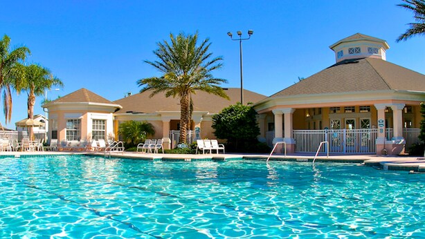 A swimming pool with lounge chairs and palm trees, surrounded by buildings with a classic architectural style. - Windsor Palms 8112 (Kissimmee)