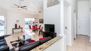 A spacious living room with a large TV, comfortable seating, a dining area with red chairs, and a view of the outdoors. - Tuscan Hills 353 (Davenport)