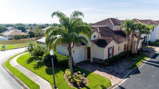 A residential house with a curved driveway, palm trees, and a well-maintained lawn. - Tuscan Hills 353 (Davenport)