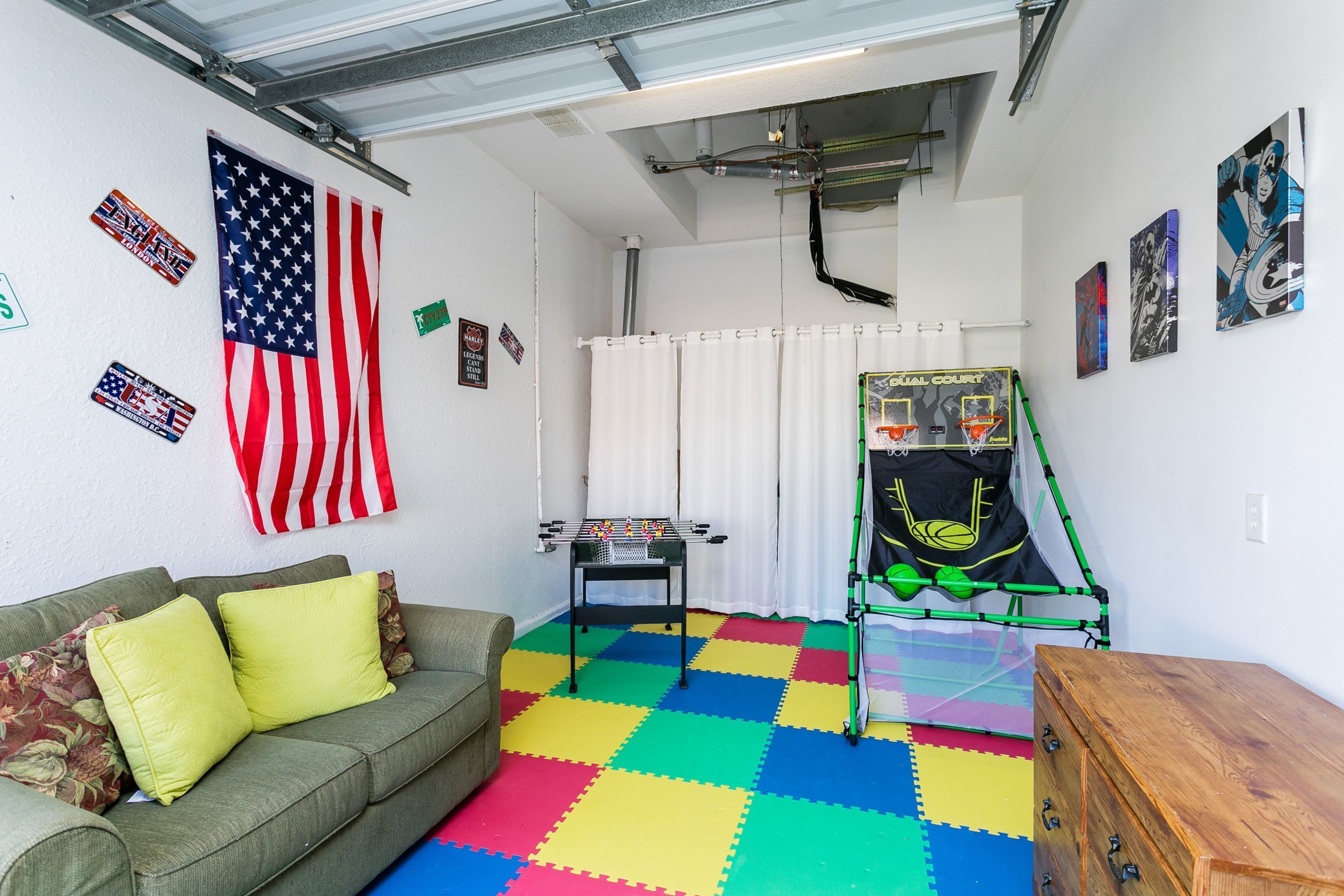 Una habitación con un sofá verde, piso de espuma de colores, una bandera estadounidense y una mesa de futbolín.