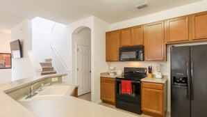 A modern kitchen with wooden cabinets, a black refrigerator, a microwave, and a stove. - Bella Vida 4572 (Kissimmee)