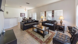A spacious living room with two black leather sofas, a glass coffee table, and a patterned rug. There are two lamps on side tables, and a flat-screen TV mounted on the wall. - Bella Vida 4572 (Kissimmee)