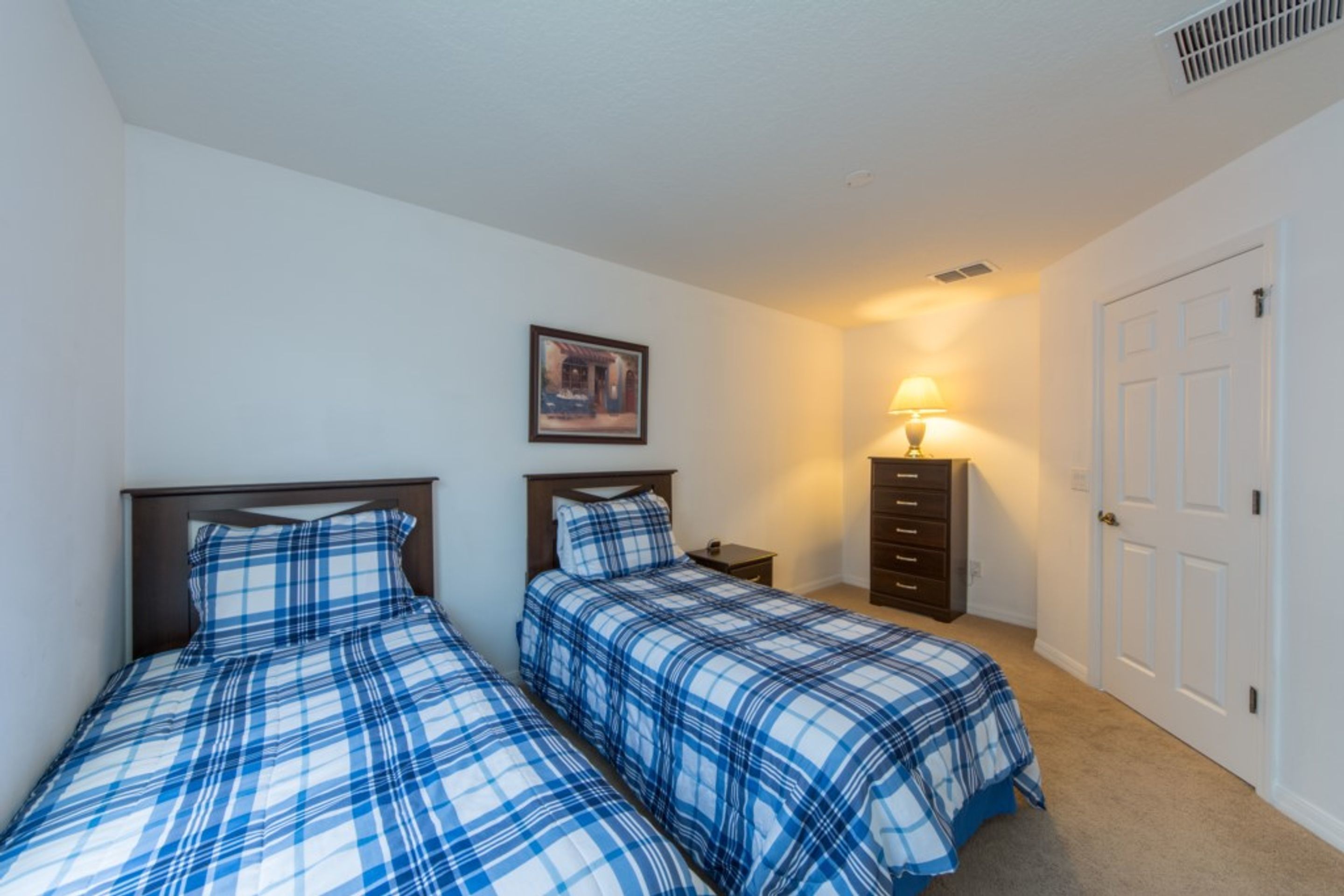 A bedroom with two beds, a nightstand, a dresser, a lamp, and a door.
