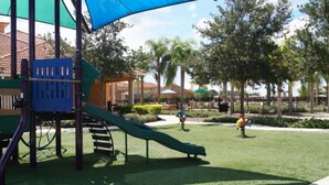 A playground with a slide and climbing structures, surrounded by trees and a fenced area. - Bella Vida 4572 (Kissimmee)