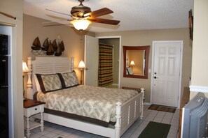 A bedroom with a bed, bedside lamps, a ceiling fan, a door, and a wall-mounted mirror.