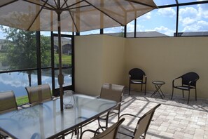 A patio with a glass table and chairs, a small round table, and a large umbrella. - Compass Bay 3149 (Kissimmee)