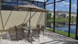Eine Terrasse mit Tisch und Stühlen, einer Glaskonstruktion und Blick auf ein Gebäude sowie ein Gewässer.