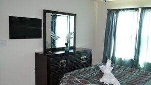 Ein Hotelzimmer mit Bett, Schminktisch, Flachbildfernseher, Spiegel und einem Fenster mit Vorhängen.