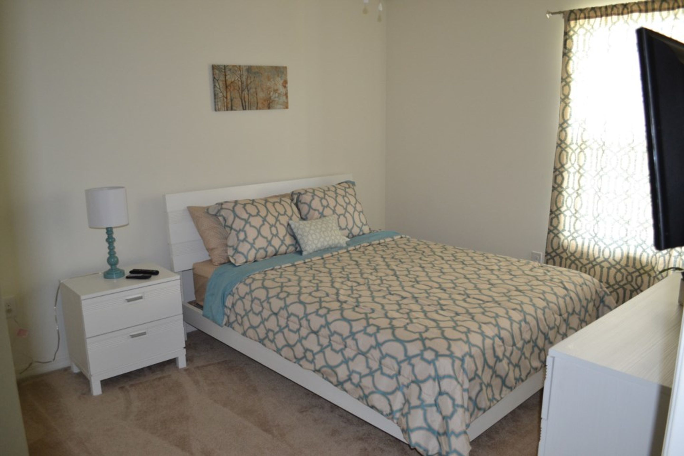 A bedroom with a bed, a nightstand, a lamp, and a window with curtains.