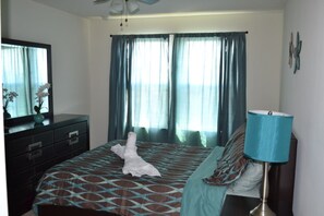 A hotel room with a bed, a dresser, a mirror, a lamp, and curtains. - Compass Bay 3149 (Kissimmee)
