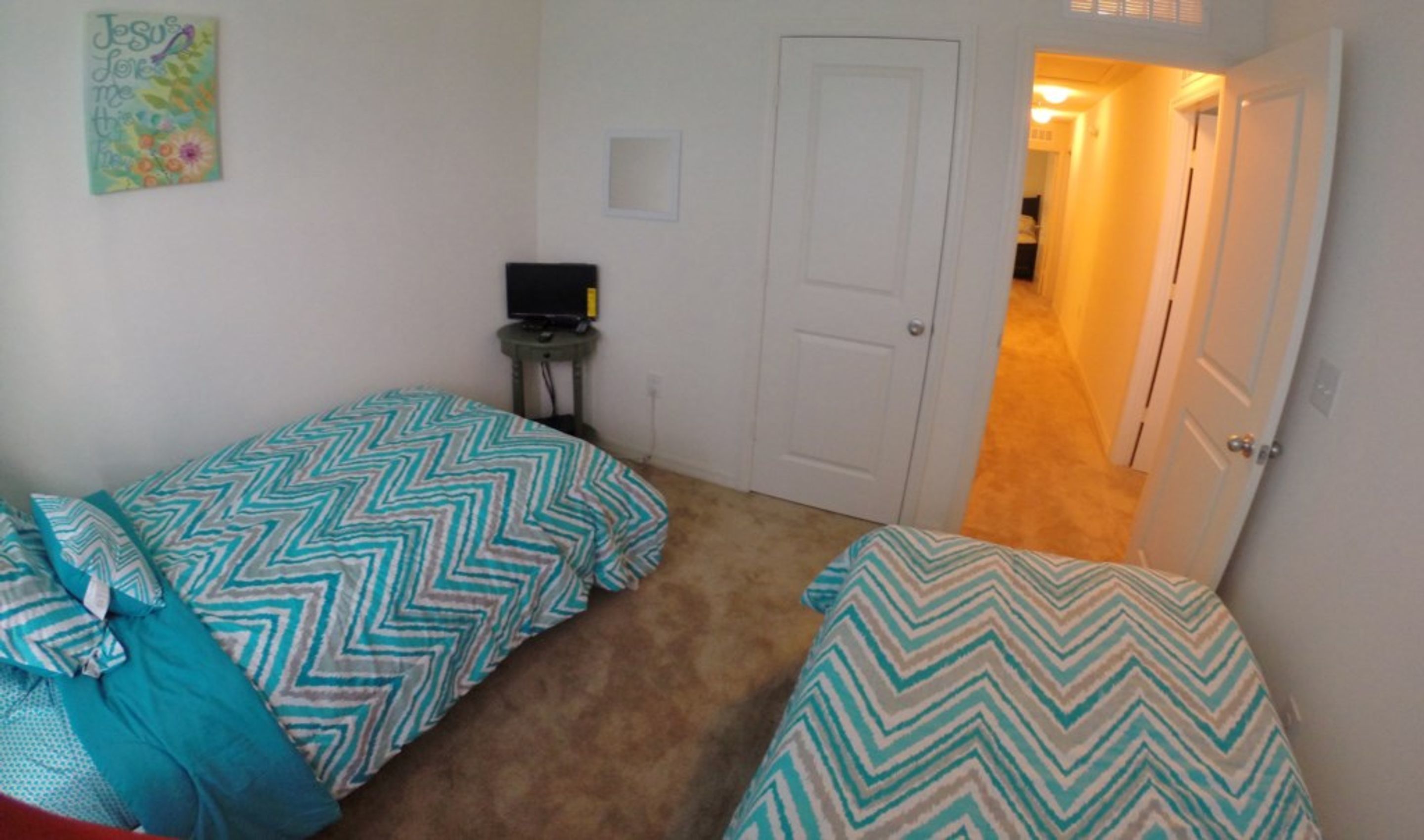 A bedroom with two beds, a small table with a TV, and a door leading to another room.