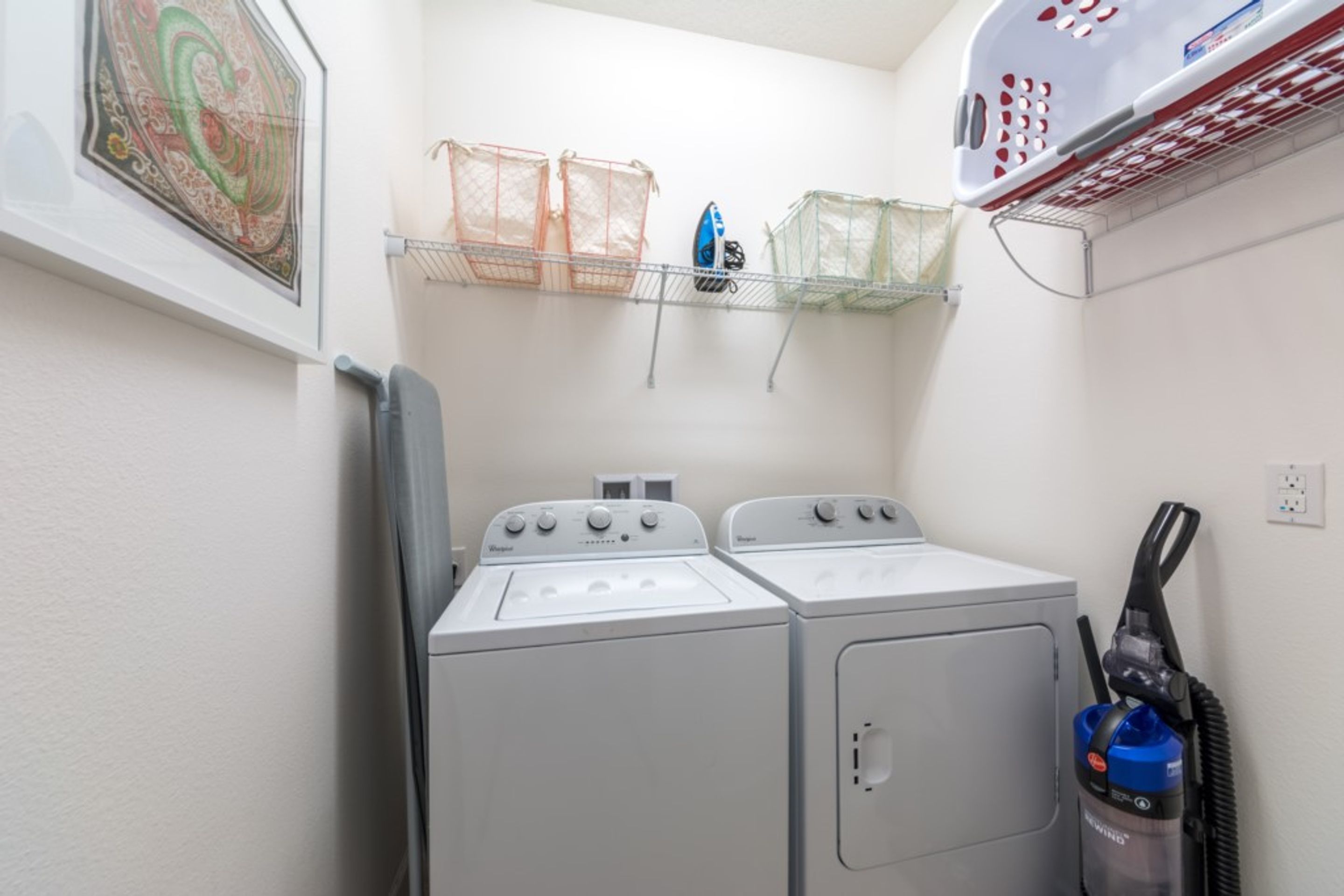 A laundry area with two front-loading washers, a drying rack, and a vacuum cleaner.