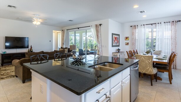 A modern kitchen with a central island, white cabinetry, and a dining area with a table and chairs. - Bella Vida 4507 (Kissimmee)