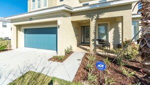 A modern two-story house with a blue garage door, a covered porch, and a landscaped front yard with a palm tree and shrubs. - Bella Vida 4507 (Kissimmee)
