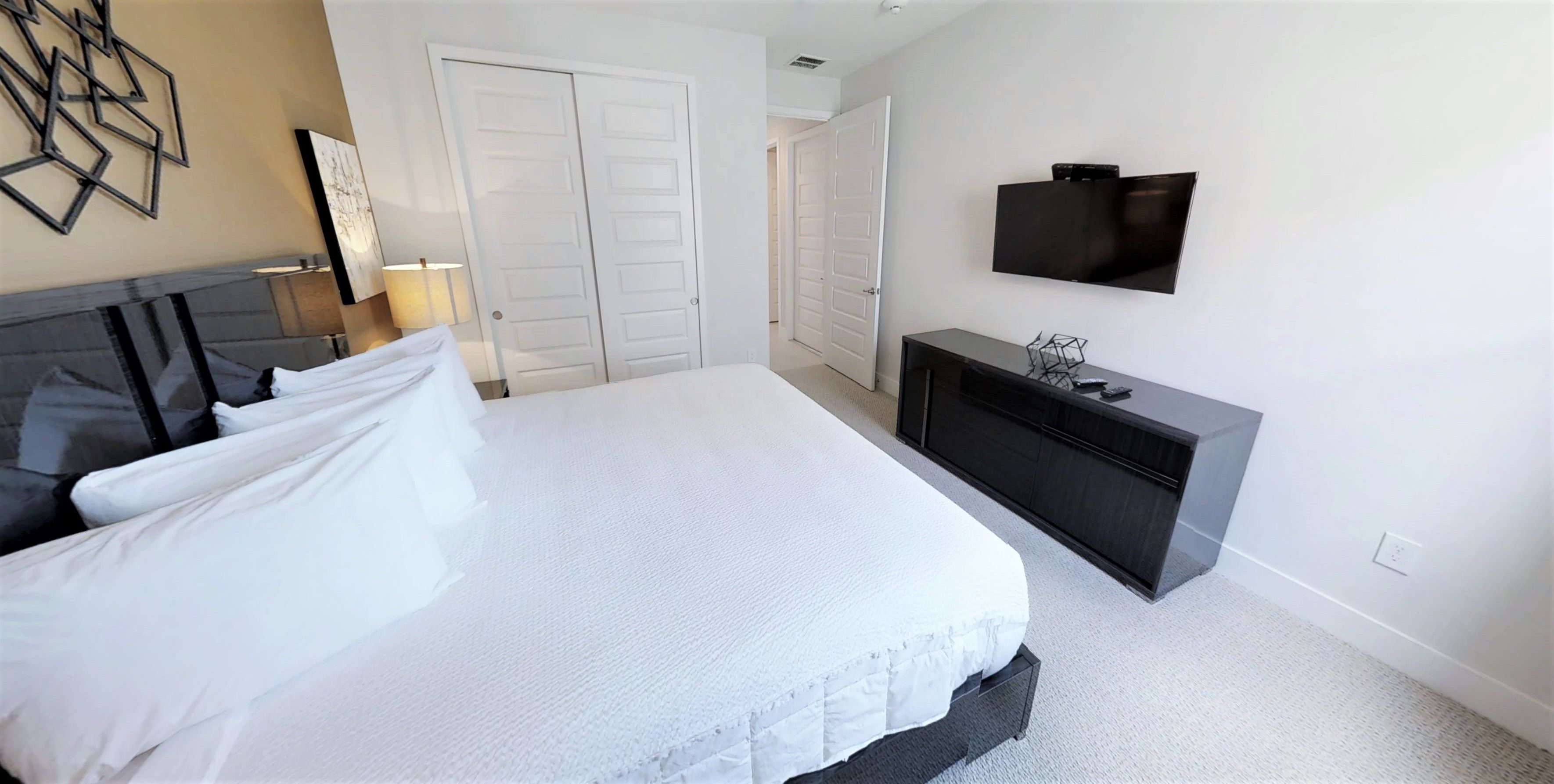 A bedroom with a large bed, a dresser, a TV, and two doors.