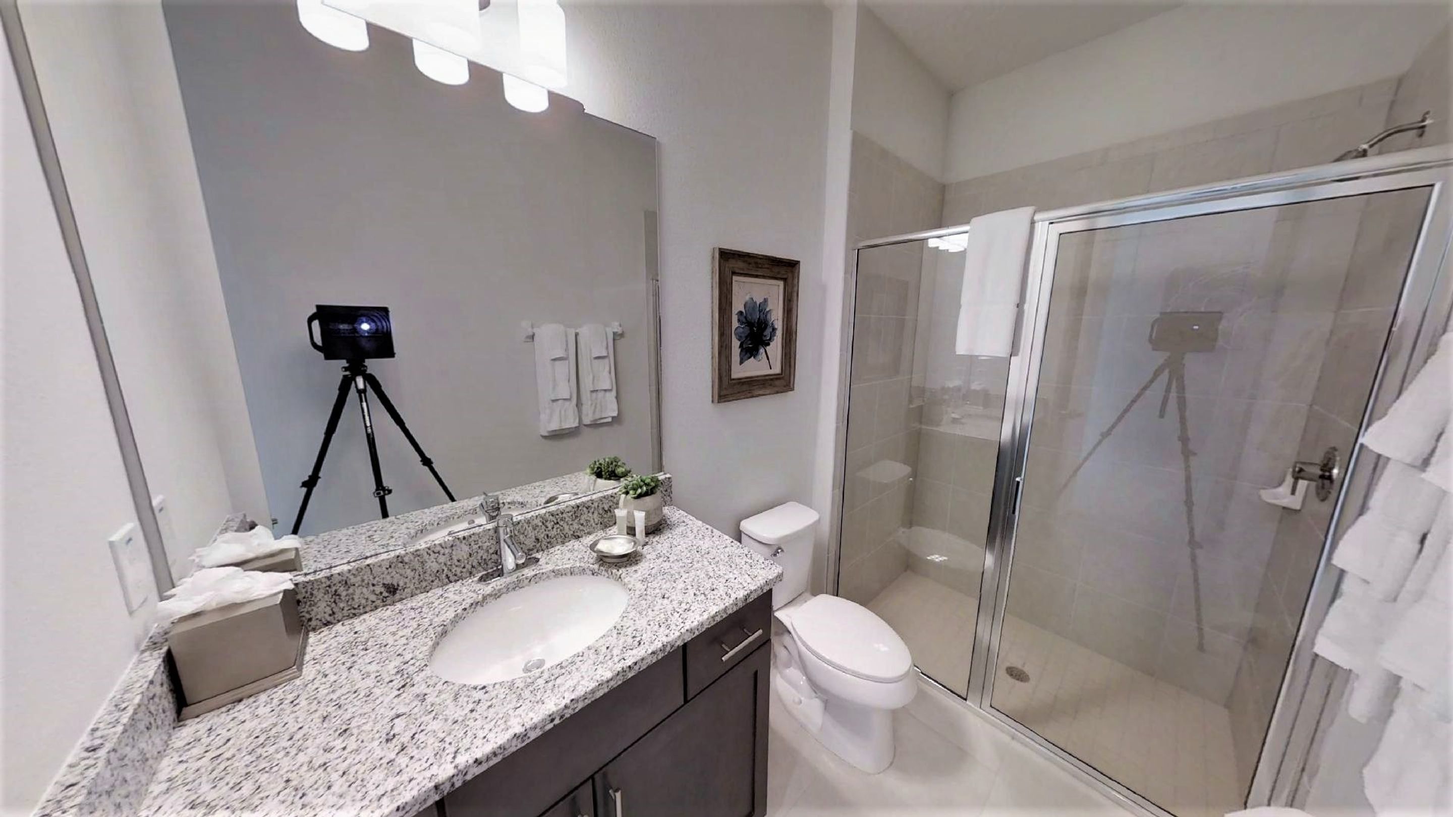 Un baño moderno con encimera de granito, un espejo grande, un inodoro y una ducha con mampara de vidrio.