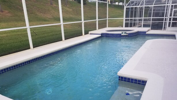 Ein Swimmingpool mit klarem, blauem Wasser, umgeben von einer weißen Sonnenterrasse und einer Glaseinfriedung.