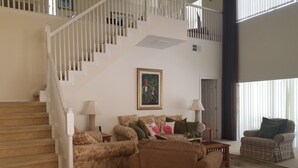 Ein Wohnzimmer mit Treppe, einer Sofagarnitur, einem Sessel und einem Gemälde an der Wand.