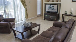 Ein Wohnzimmer mit braunen Ledersitzen, einem dunklen Holztisch und einem Fernseher auf einem Standfuß, der 'Florida Vacation Homes' anzeigt.