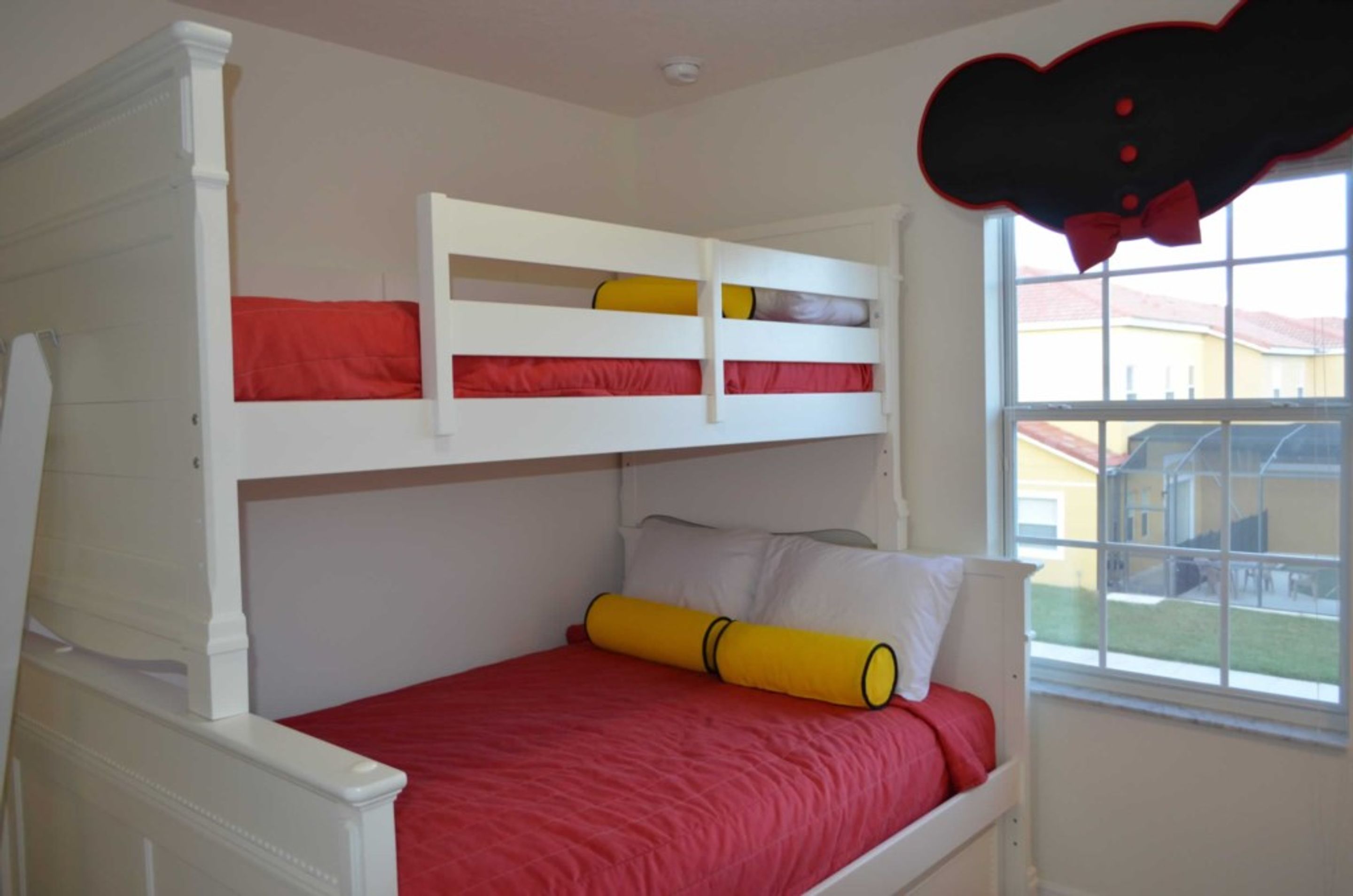 Un lit superposé avec une literie rouge et une fenêtre donnant sur une maison.