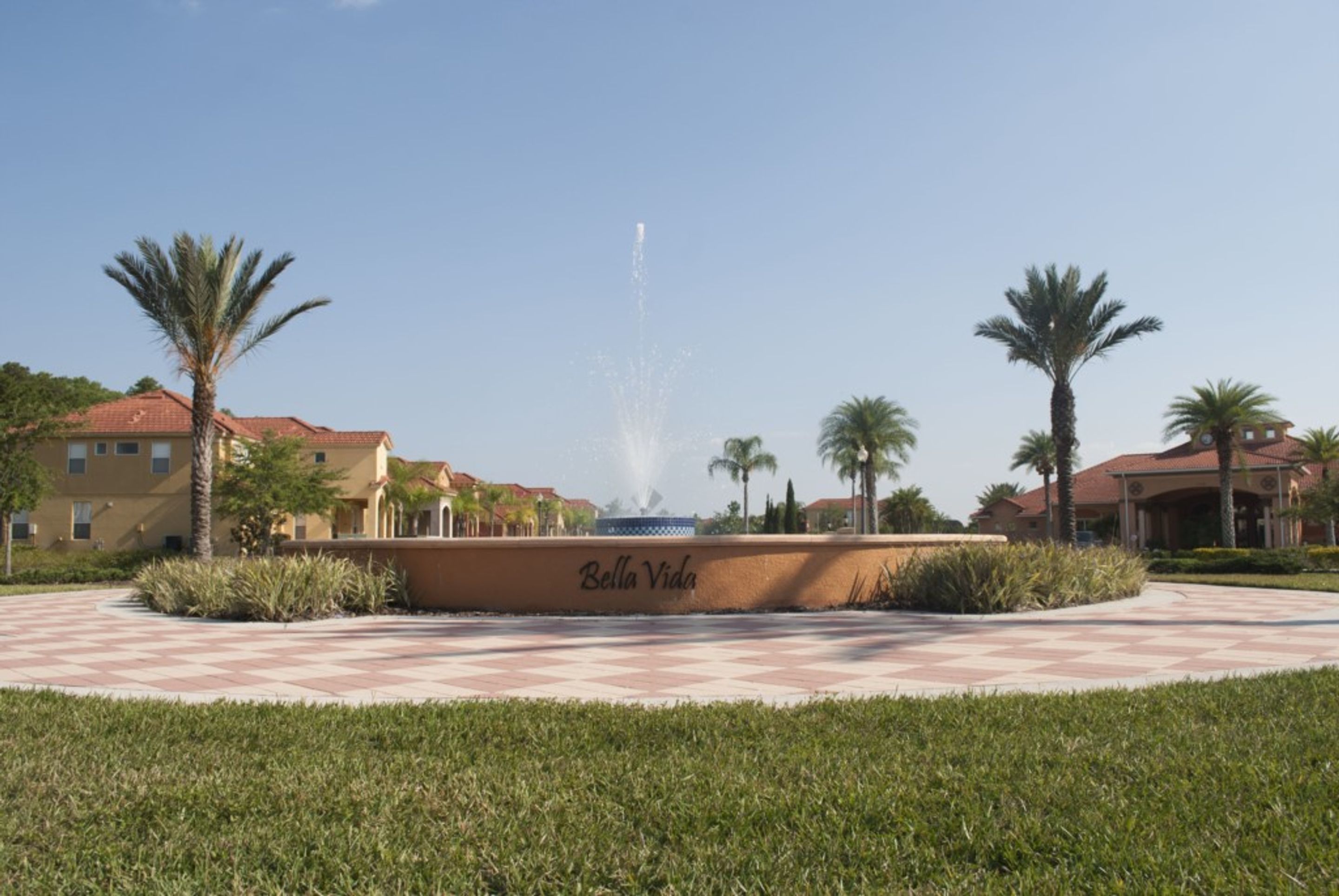 A fountain in a courtyard with palm trees and buildings labeled "Bella Vida".