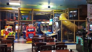 Un espace de jeux intérieur comprenant divers jeux d’arcade, une structure d’escalade et des sièges pour les adultes.
