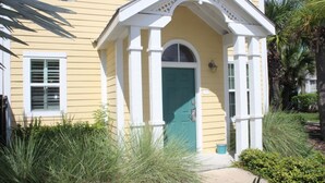 Una casa amarilla con puerta verde, detalles blancos y un pequeño porche.