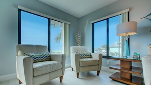 Ein modernes Wohnzimmer mit zwei Sofas, einem Holztisch und großen Fenstern mit Blick auf Palmen und eine Stadtlandschaft.