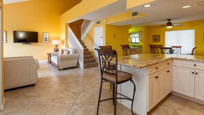 Un salón comedor amplio con isla de cocina y una escalera que sube a un nivel superior.