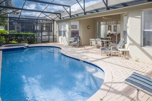 A swimming pool with a glass enclosure, surrounded by patio furniture and a covered seating area.