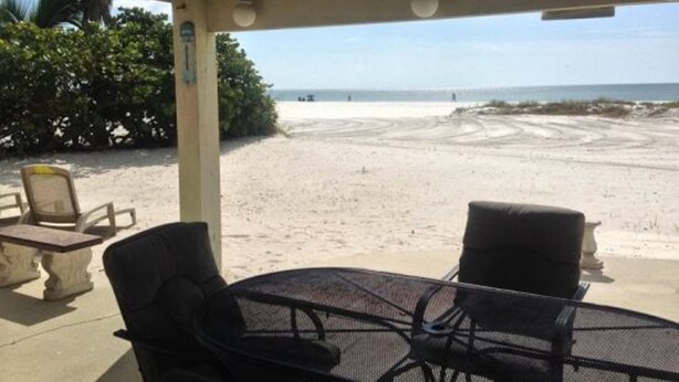 Un espace extérieur abrité, aménagé avec des sièges, et offrant une vue sur une plage de sable et l’océan.