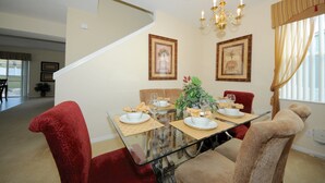 A dining area with a glass table, red and beige chairs, framed artwork on the wall, and a chandelier. - Legacy Park 120 (Davenport)