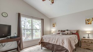 Une chambre à coucher comprenant un lit, des tables de chevet, un bureau avec une télévision et une fenêtre.