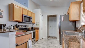 Une cuisine dotée de meubles en bois, d’un four à micro-ondes, d’une cuisinière, d’un réfrigérateur, de plans de travail en granit et d’une porte donnant sur une autre pièce.