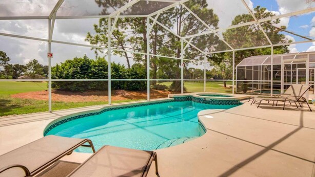 Une piscine extérieure couverte, dotée de chaises longues, d’un jacuzzi et offrant une vue sur un terrain de golf.