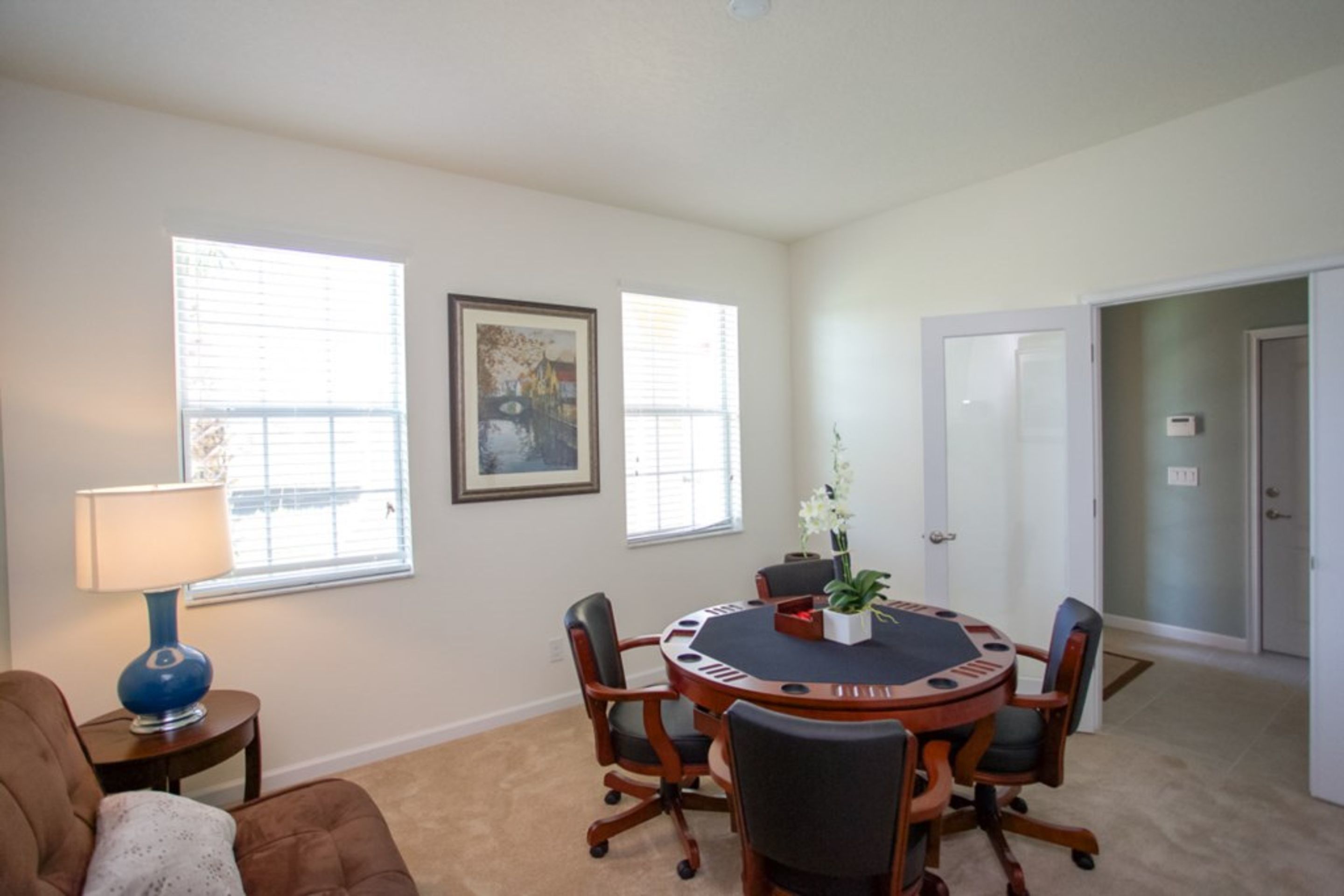 A conference room with a round table, six chairs, a blue lamp, and two windows with blinds.