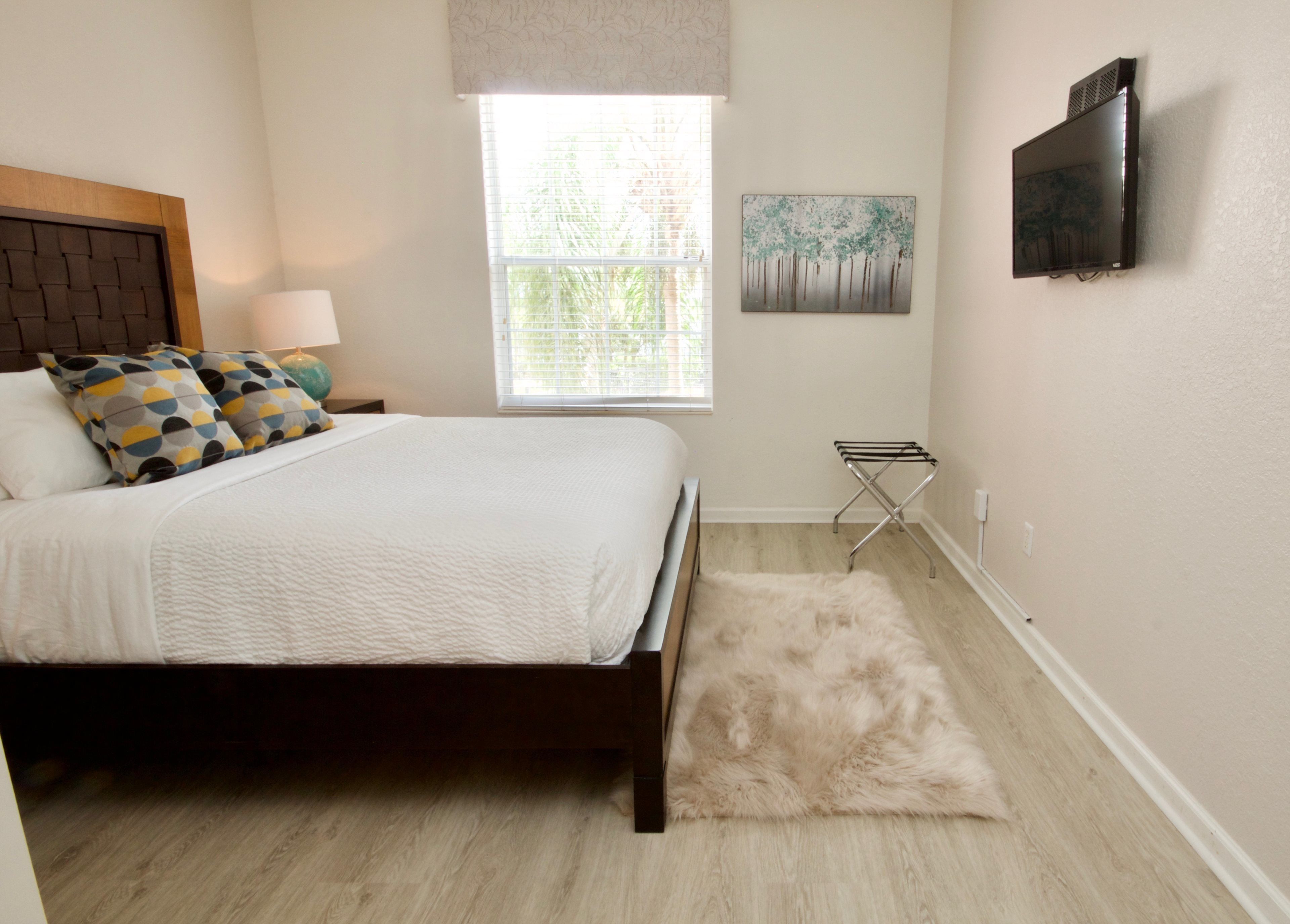 Un dormitorio con una cama, una ventana, un televisor montado en la pared y un cuadro.