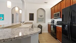 A modern kitchen with granite countertops, wooden cabinets, a black refrigerator, and a microwave. - Vista Cay 4862 - 202 (Orlando)