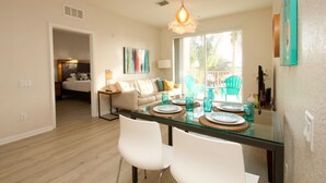 A modern dining area with a glass table, white chairs, and a view of the outdoors. - Vista Cay 4862 - 202 (Orlando)