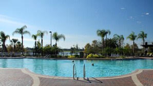 A swimming pool with a tiled deck, palm trees, and a clear sky. - Vista Cay 4862 - 202 (Orlando)