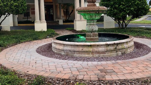 A building with a central fountain, an arched entrance, and a tiled roof. - Tuscan Hills 220 (Davenport)