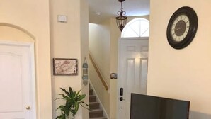 A living room with a flat-screen TV on a black stand, a potted plant, and a staircase leading to another room. - Tuscan Hills 220 (Davenport)