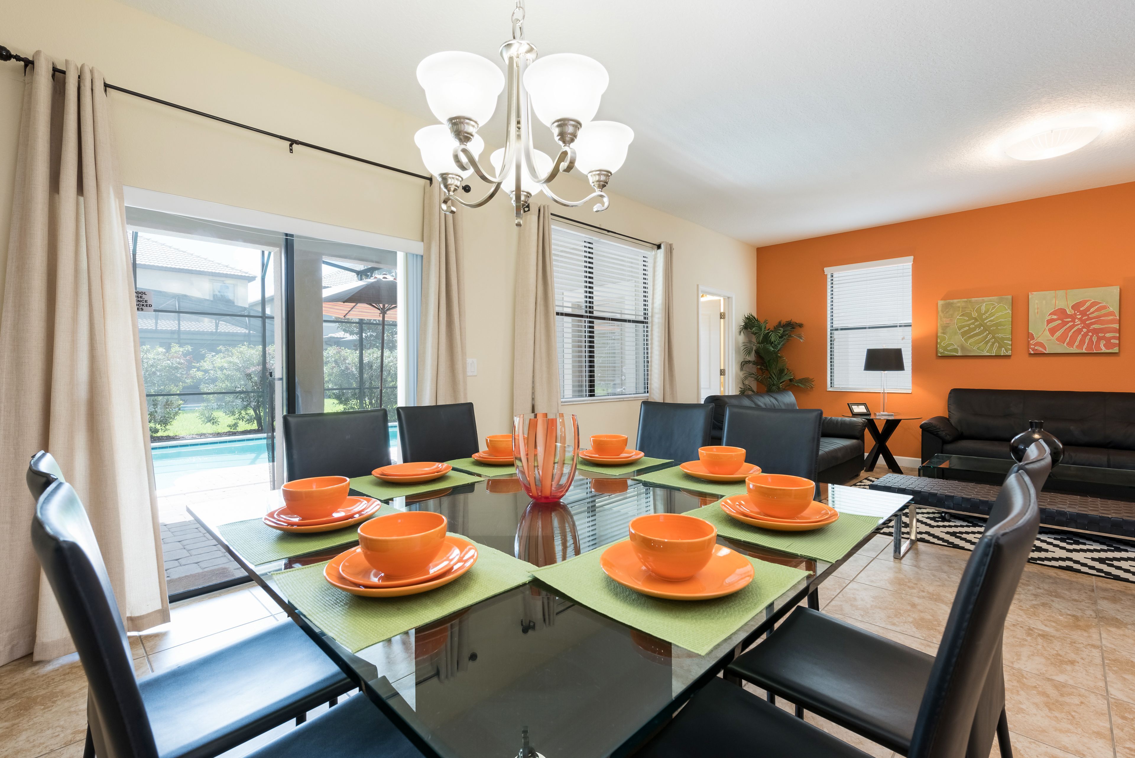 A dining area with a glass table, orange plates, and black chairs.