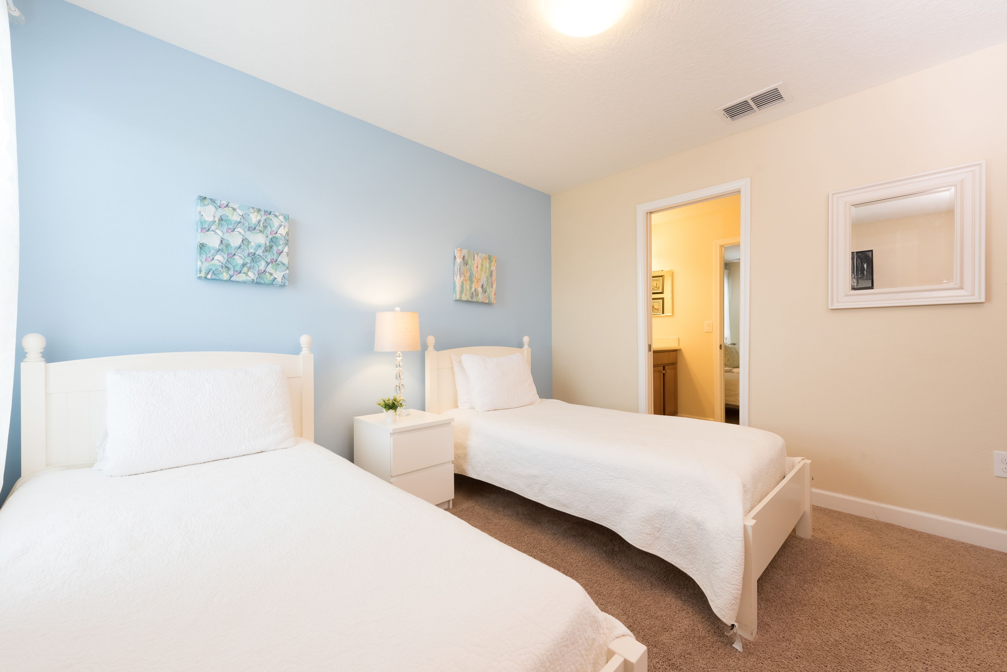 A bedroom with two single beds, a nightstand with a lamp, and two wall-mounted paintings.