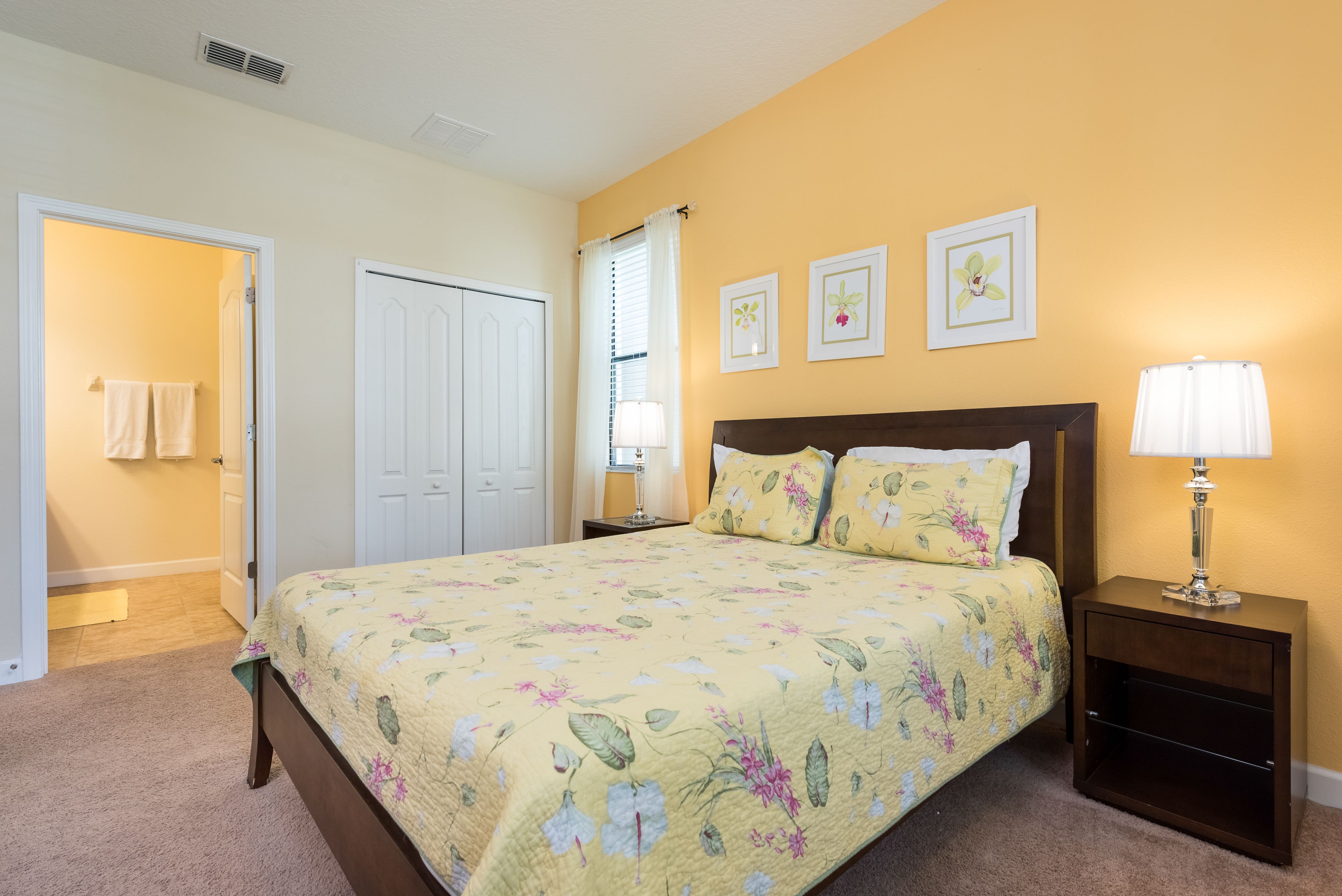 A bedroom with a floral bedspread, a nightstand with a lamp, and a door leading to a bathroom.