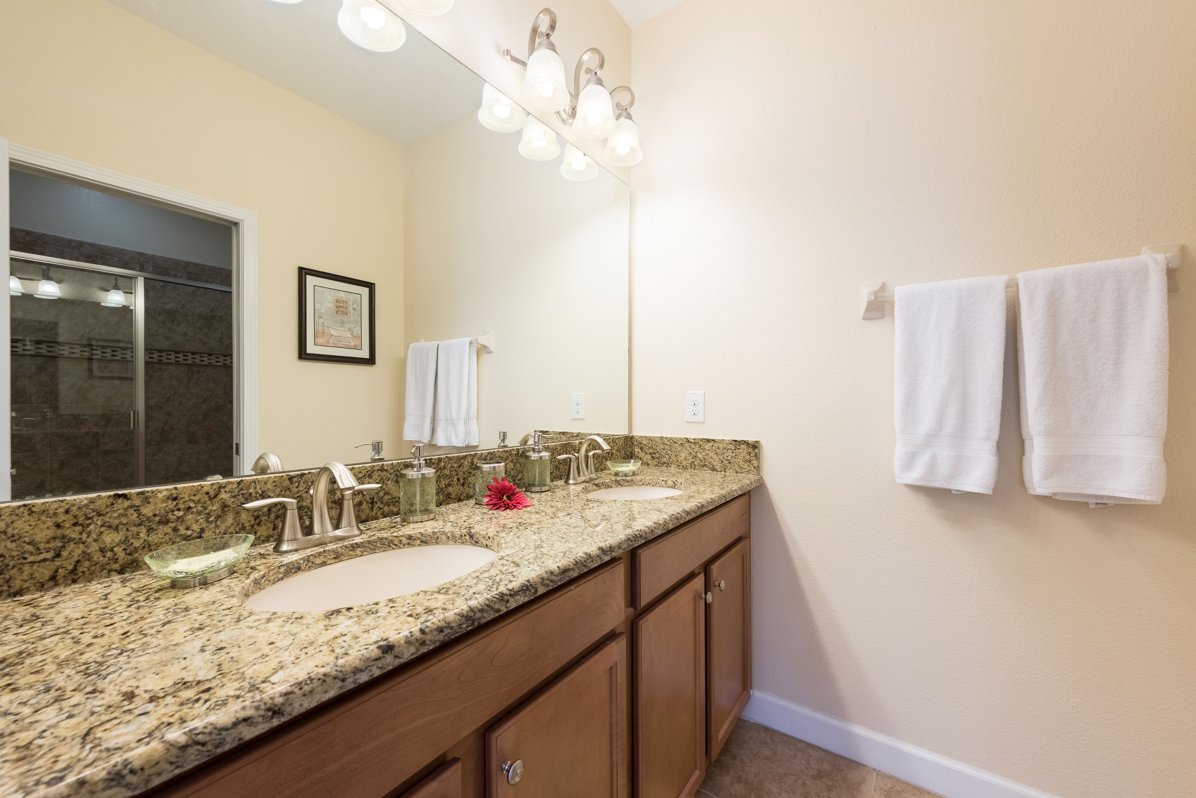 A bathroom with a granite countertop, two sinks, a large mirror, and a towel rack.