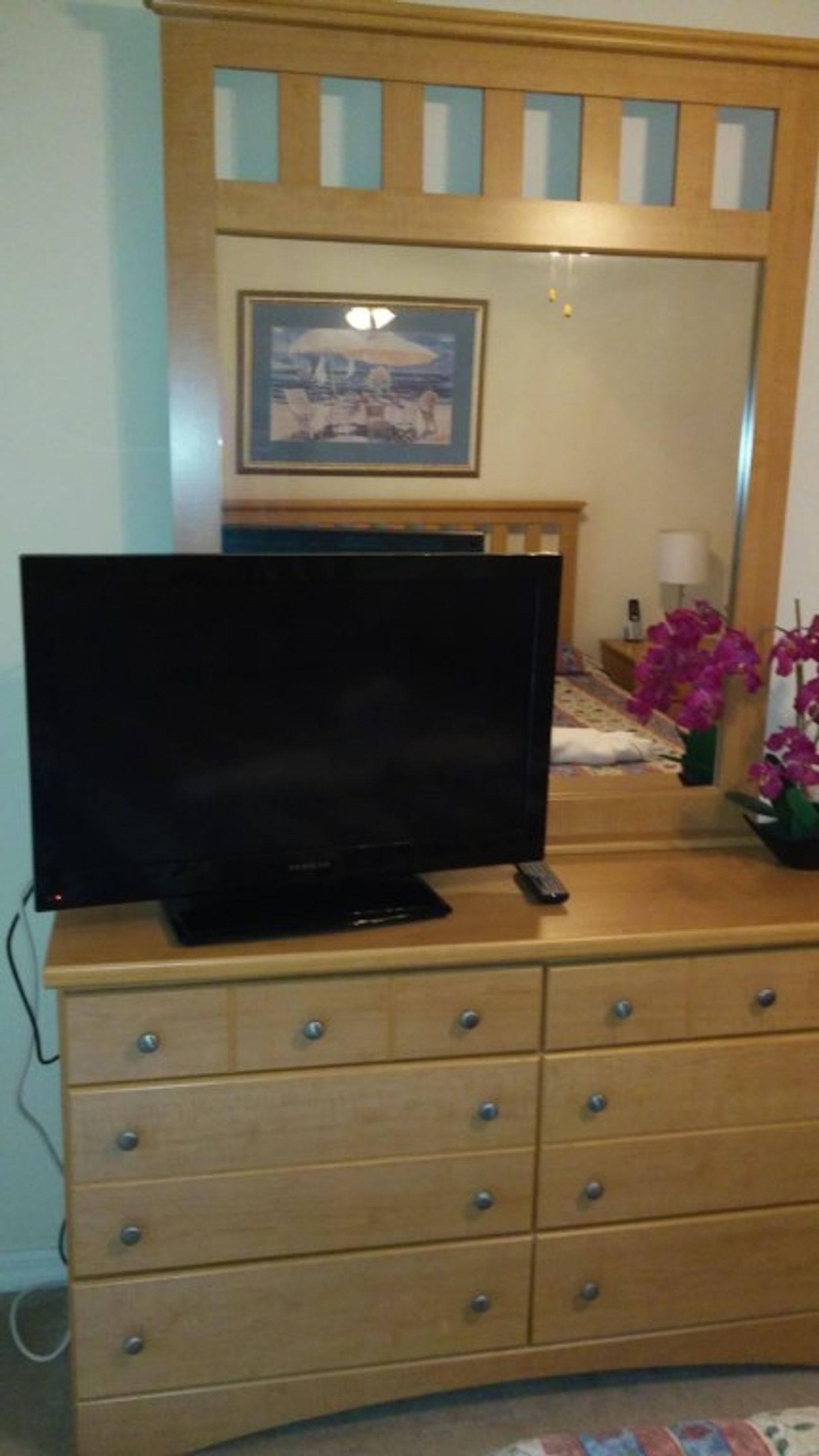 Un aparador de madera con un televisor de pantalla plana encima, un espejo sobre él y un cuadro en la pared.